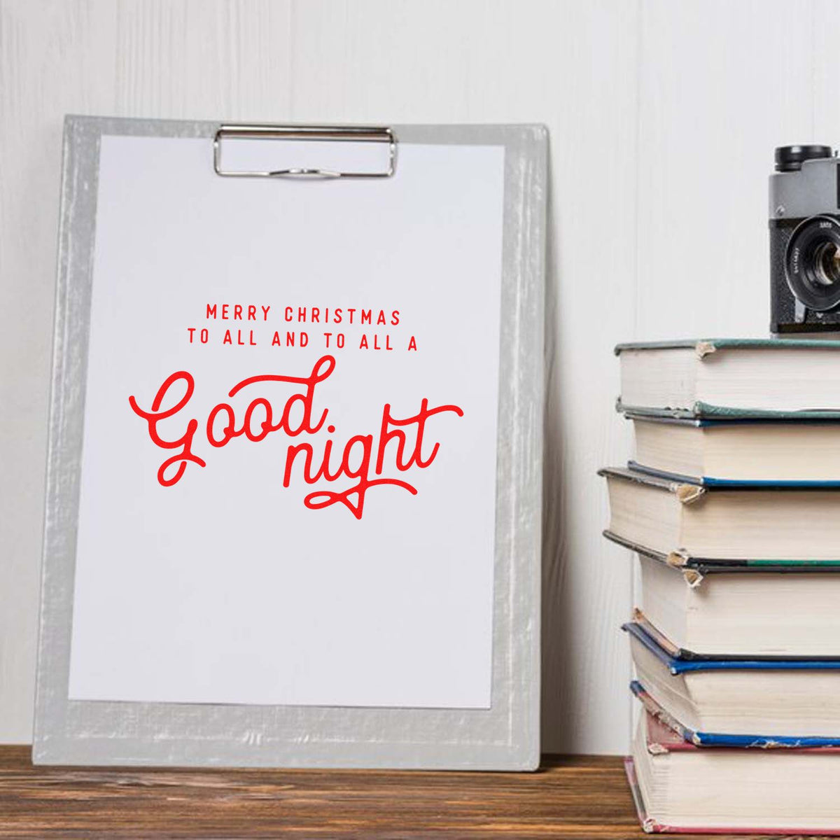 Red Christmas stamp and seal design on clipboard, with Good night script and merry message, beside stacked books.