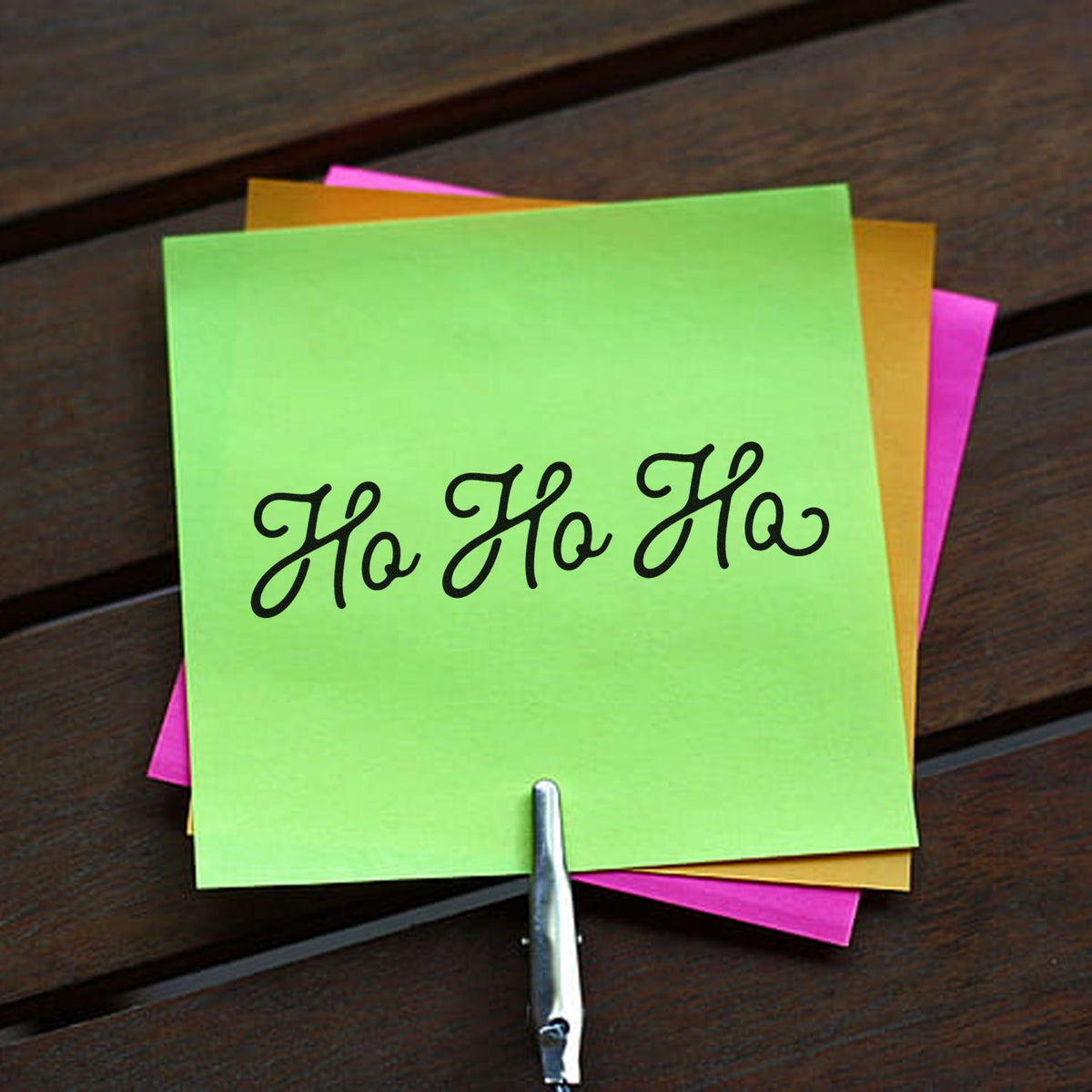 Neon green sticky note stamped Ho Ho Ho in black, with pink and gold layers and a metal stamp/seal tool.