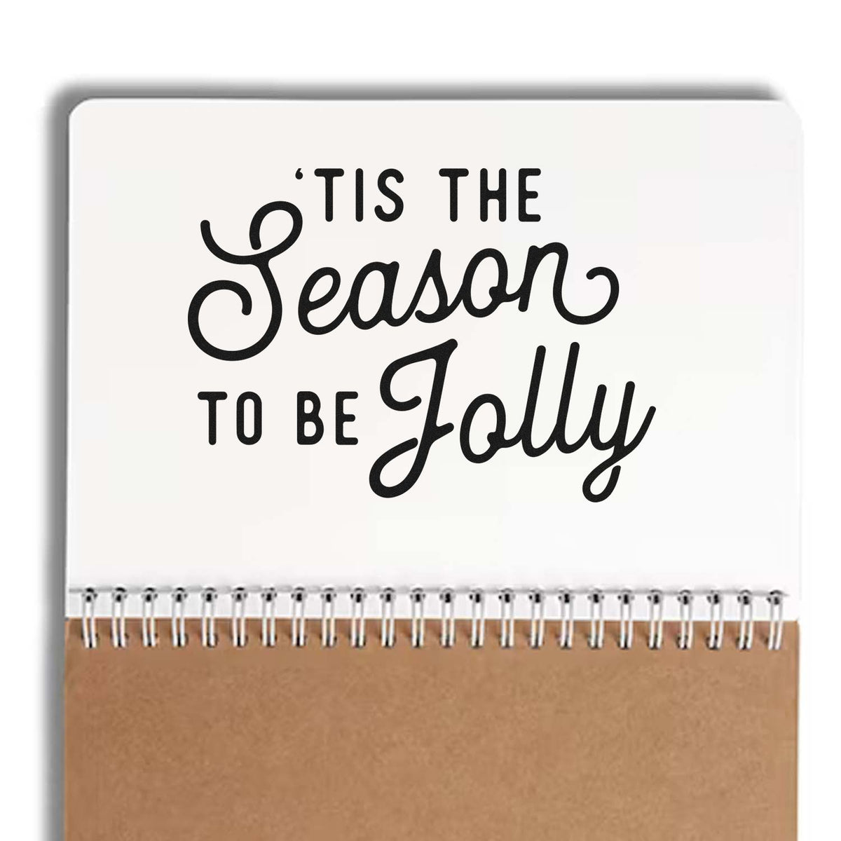 Spiral-bound holiday stamp and seal notebook with black Tis the Season to be Jolly text, white cover, and kraft brown bottom.