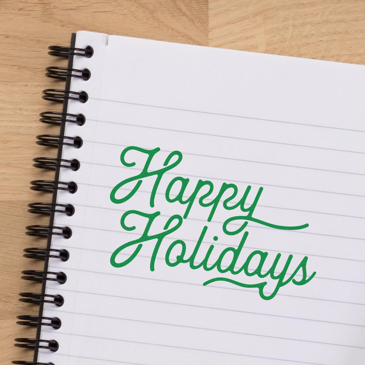 Green Happy Holidays stamp and seal design on a white lined spiral notebook with black binding.