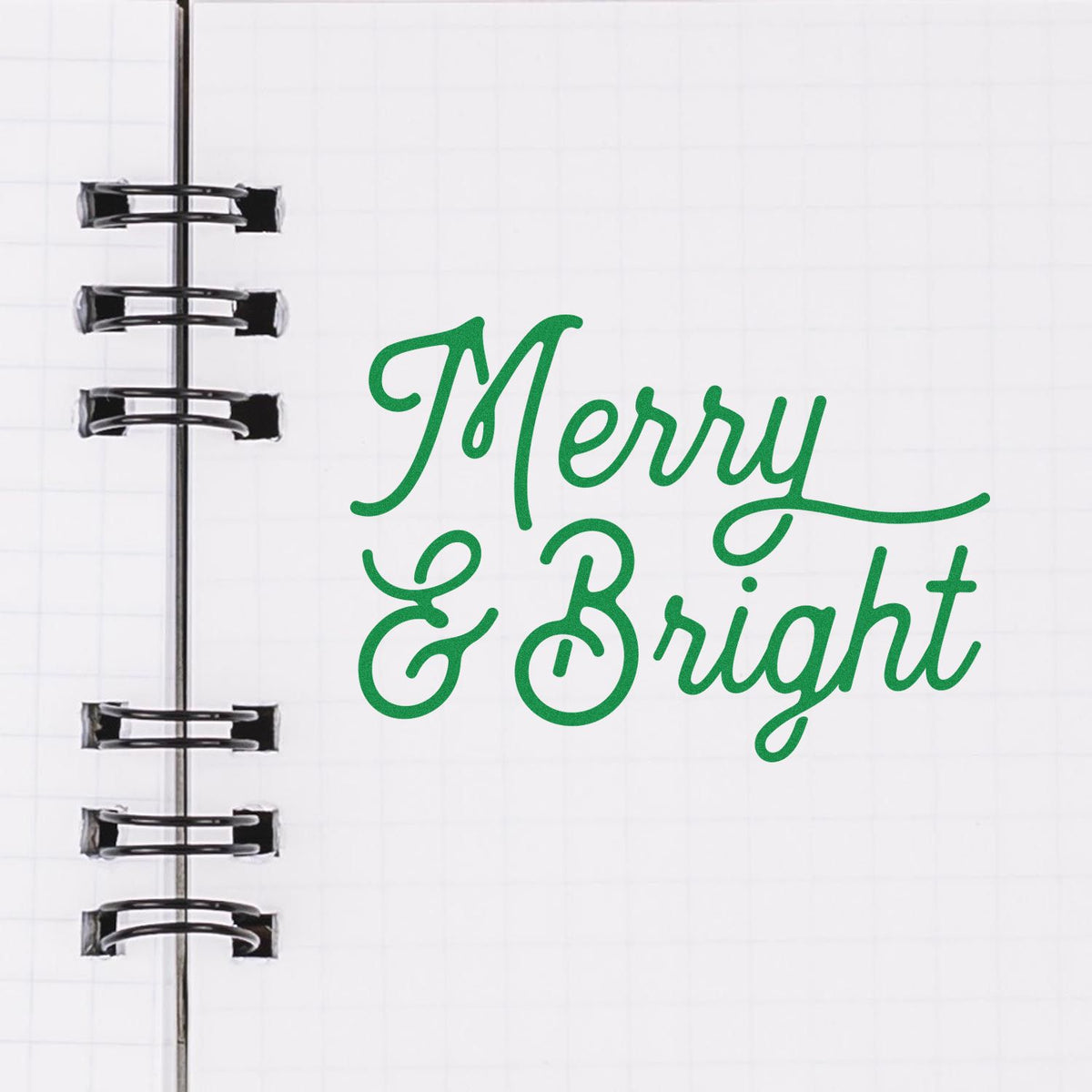 Green Merry & Bright script stamp on white notebook page beside black spiral rings