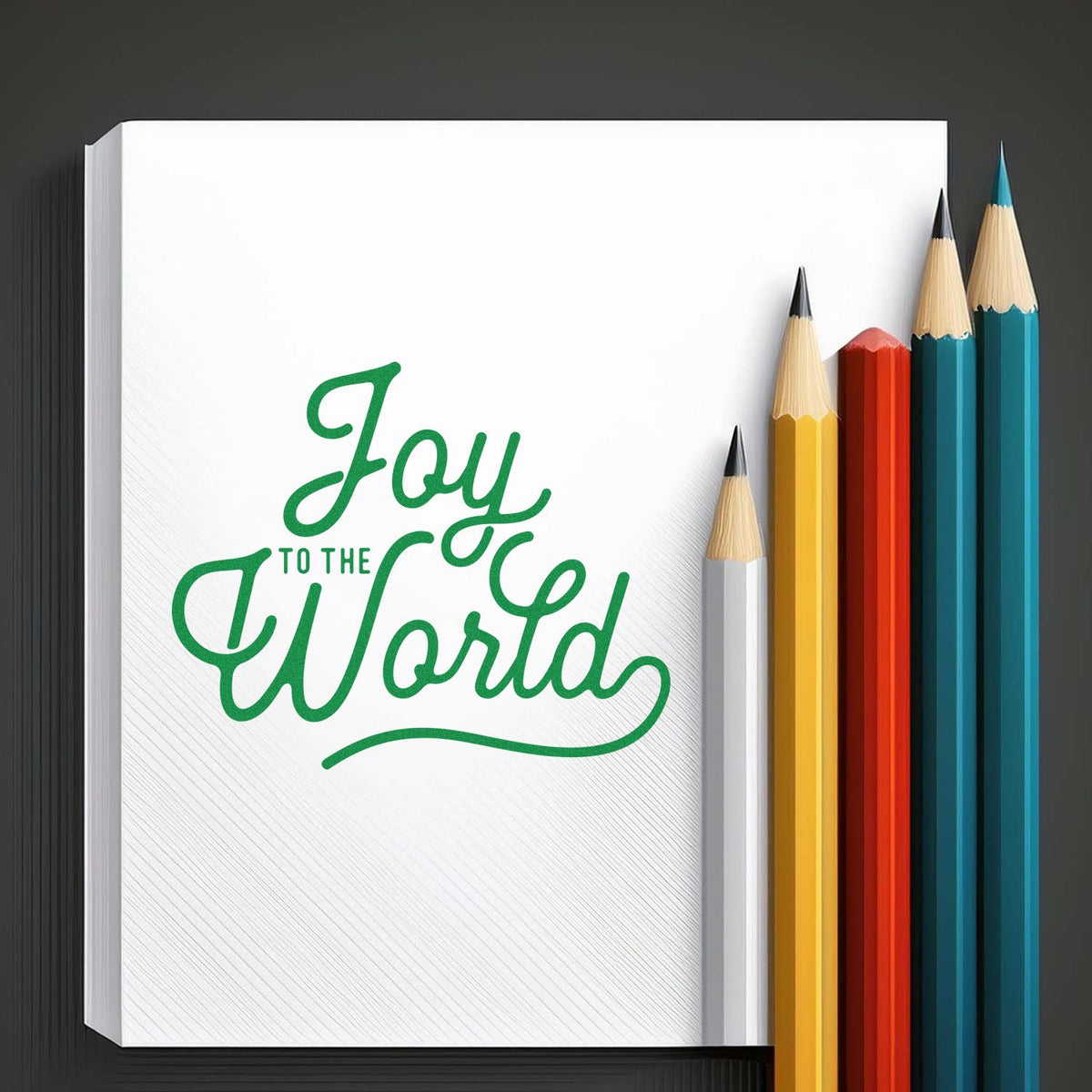 Green Joy to the World stamp design on white paper, with yellow, red, teal, and blue pencils.
