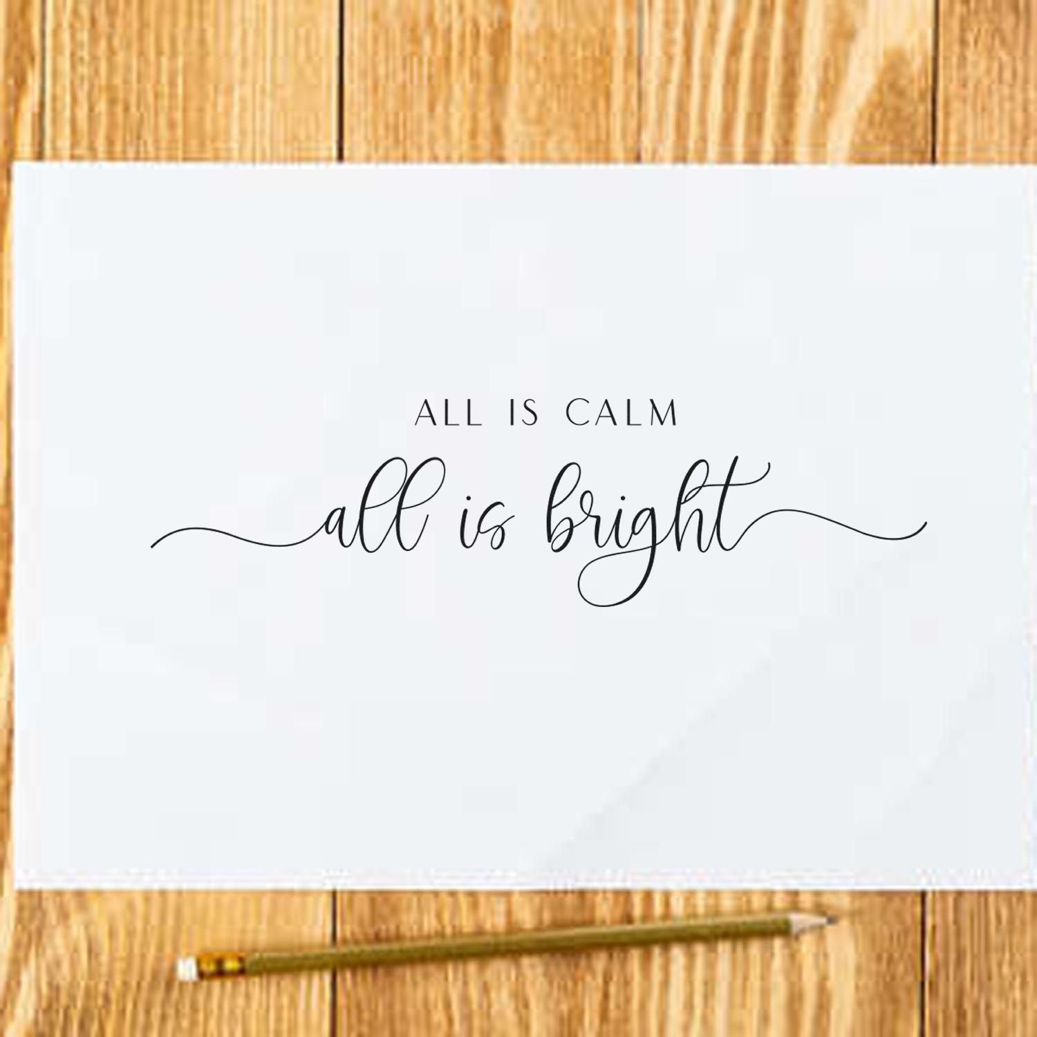 White stamp and seal card with black All is calm, all is bright lettering on a wood tabletop, pencil below.
