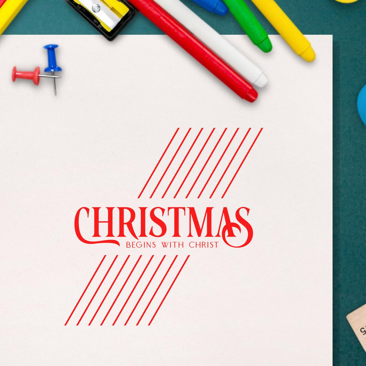 Red Christmas Begins with Christ stamp and seal design on white paper, framed by colorful markers and push pins.