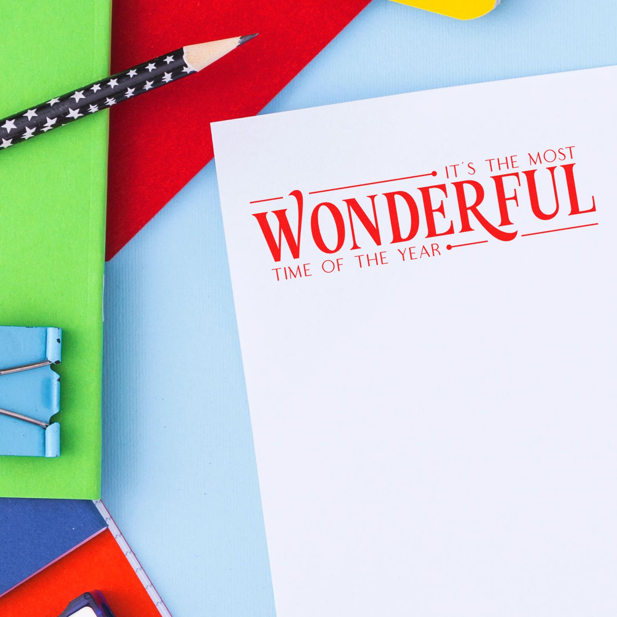 Holiday stamp and seal set with red typography on white card, star-pattern pencil, and colorful paper.