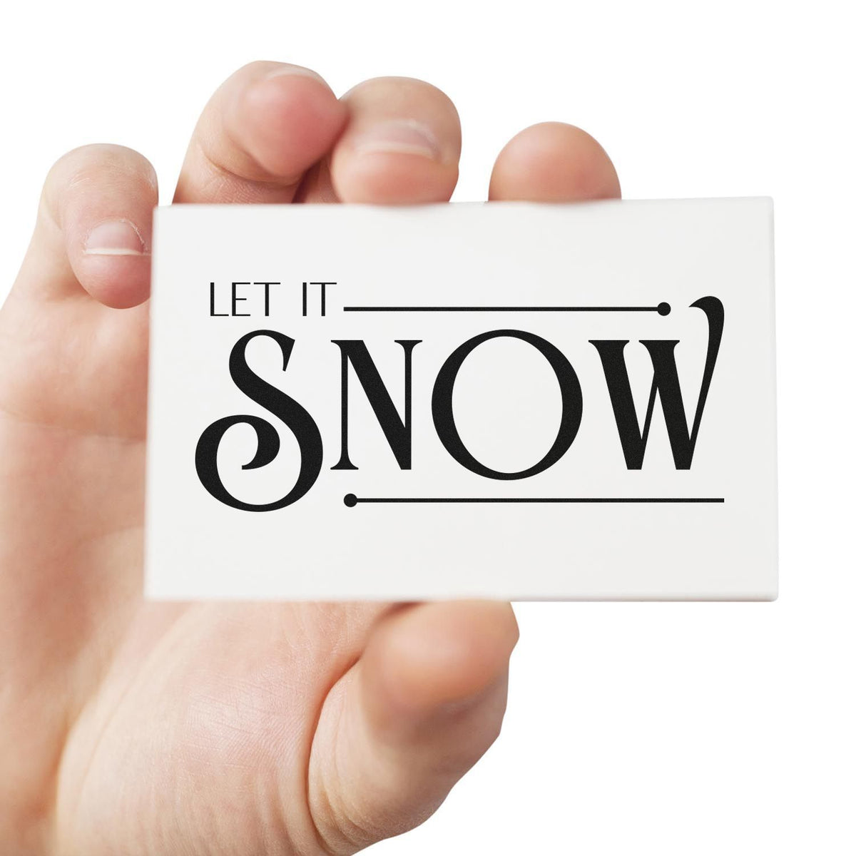 Hand holding white rubber stamp seal with black LET IT SNOW text and decorative lines