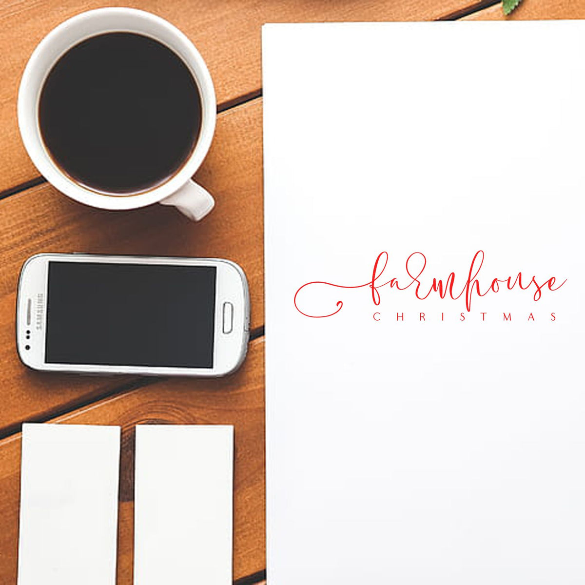 Farmhouse Christmas red seal stamp on white paper with coffee cup, smartphone, and blank cards on wood desk.