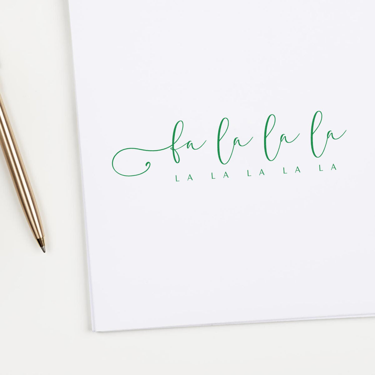 Green fa la la custom stamp on white paper with a gold pen, featuring an elegant holiday seal design.