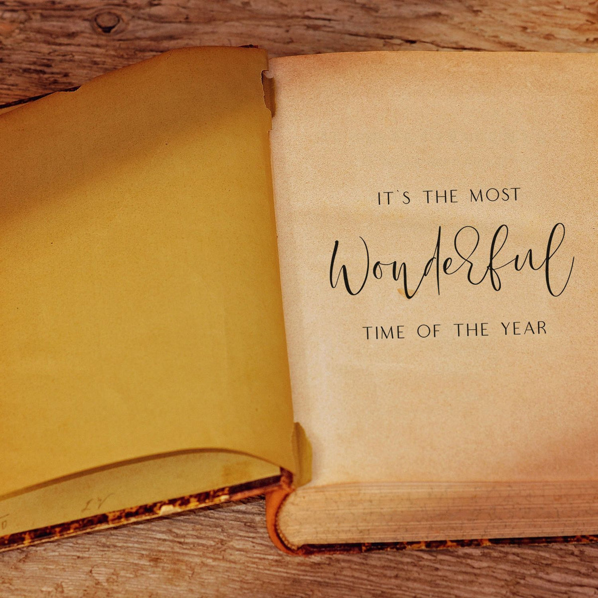 Tan stamp-and-seal book spread with black Its the most wonderful time of the year text on rustic wood.