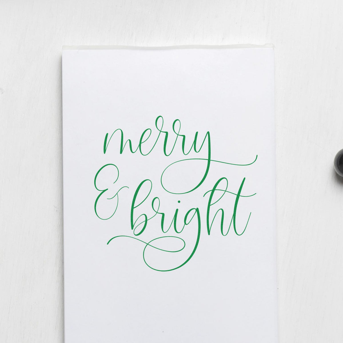 White stamp and seal packaging with green calligraphy reading merry & bright on a clean white background.