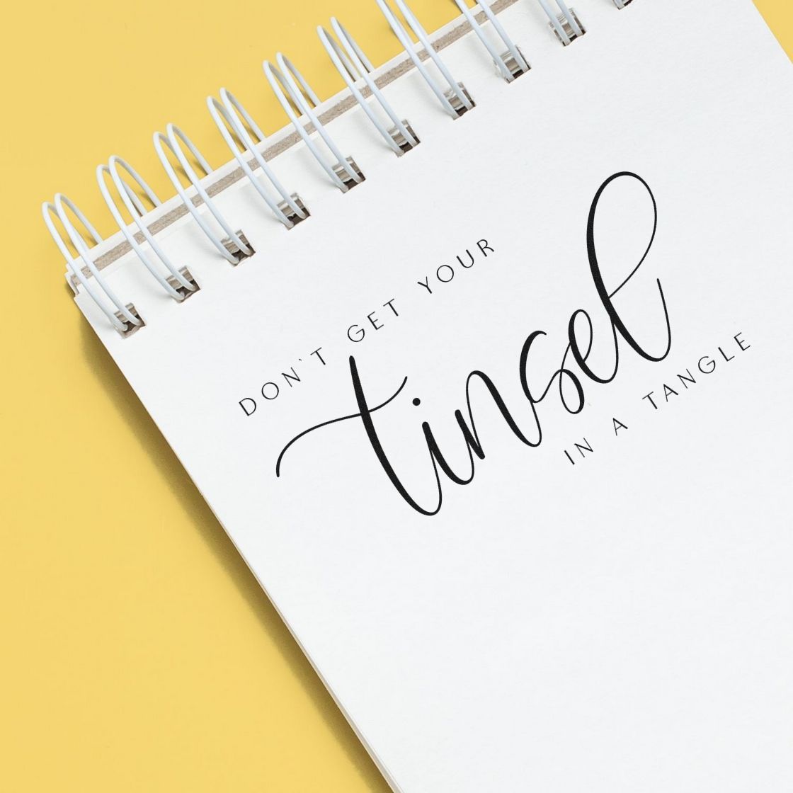 Holiday stamp and seal on white spiral notebook, black script reading Dont get your tinsel in a tangle on yellow background.