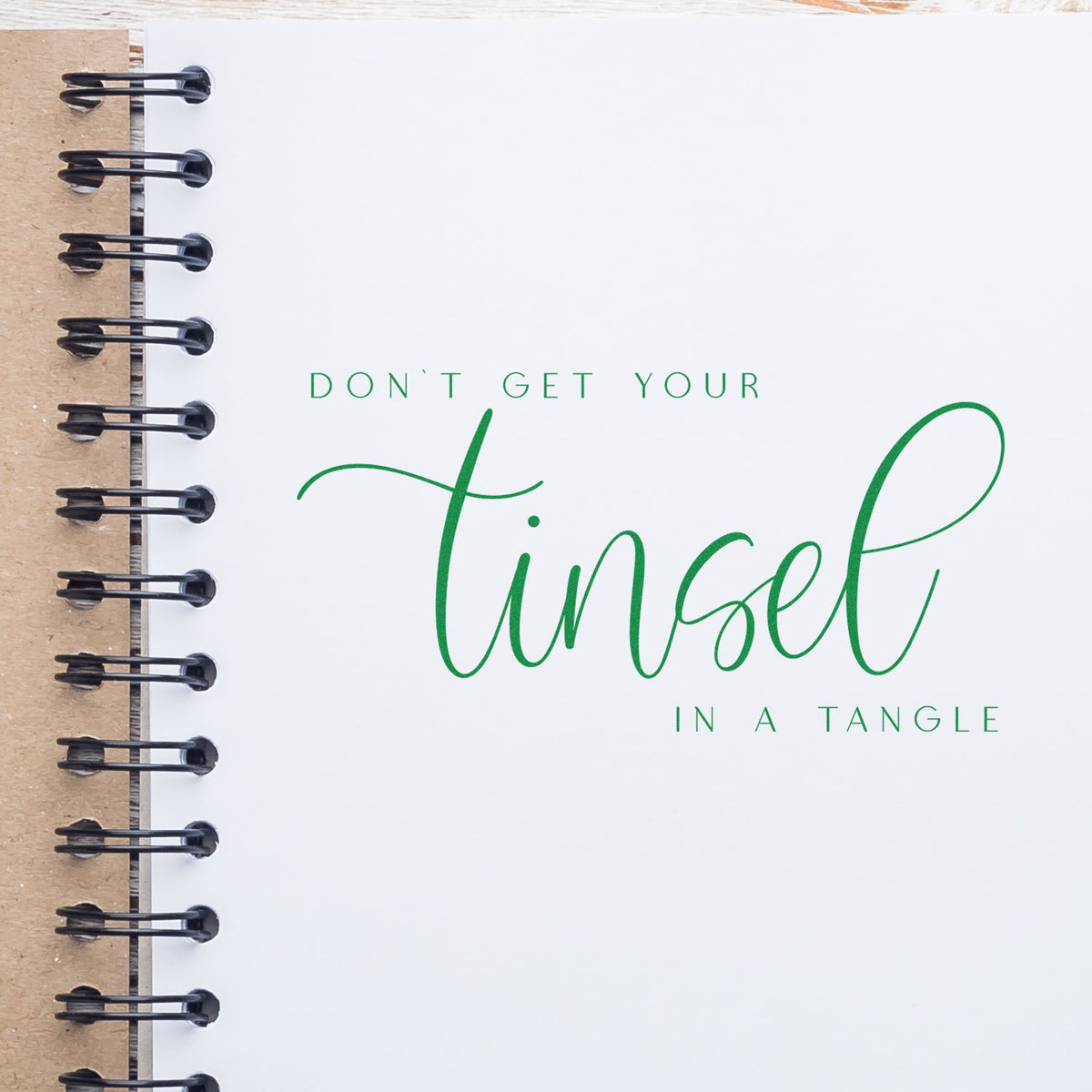 Custom stamp-and-seal design on a white spiral-bound notebook with black coil, tan kraft spine, and green lettering.