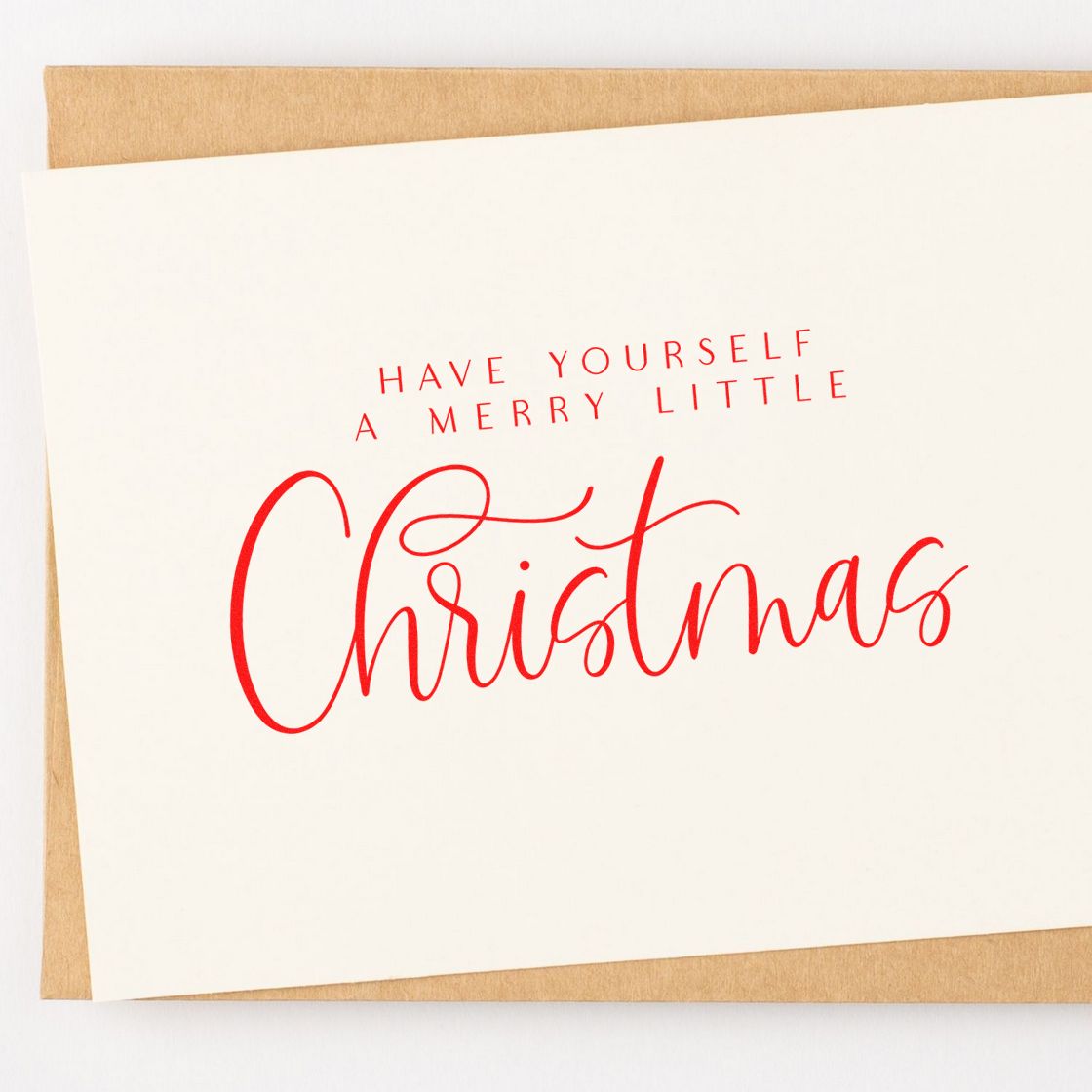 White Christmas card with red stamp-and-seal style lettering on tan kraft paper, reading Have Yourself a Merry Little Christmas.