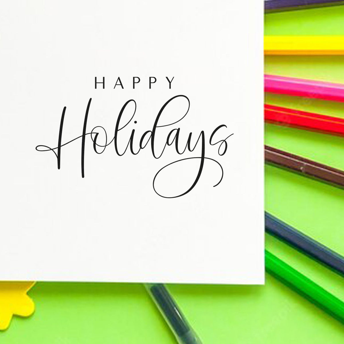 Happy Holidays black script stamp and seal on white card, with neon green, pink, yellow pencils on bright green background