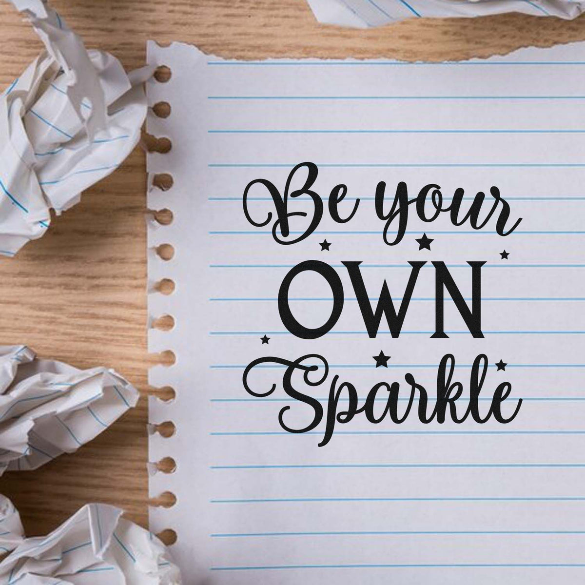 Black Be your own Sparkle stamp/seal design on lined white notebook paper, with crumpled paper accents on wood.