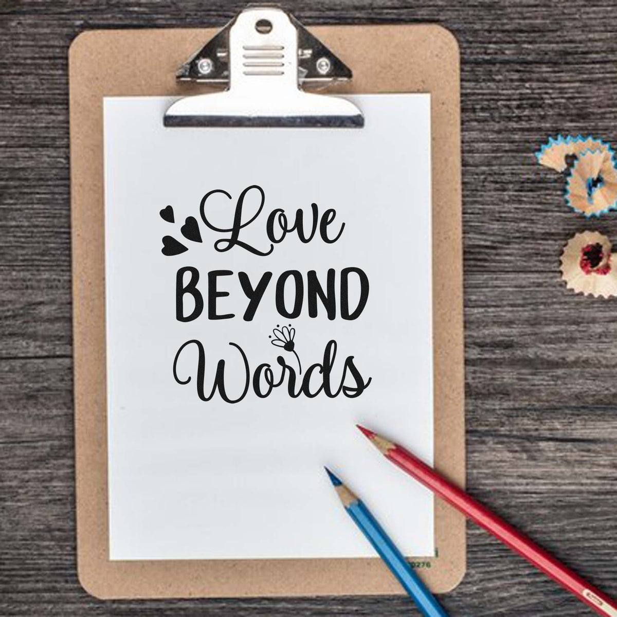 Clipboard stamp with Love Beyond Words in black script, white paper, red and blue pencils, plus decorative seal samples on wood.