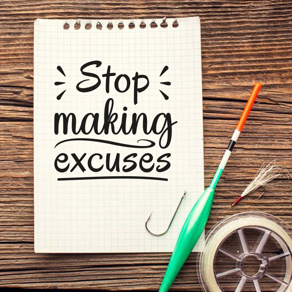 White grid notepad reading Stop making excuses in black, with green stamp/seal tool and clear spool on wood table.