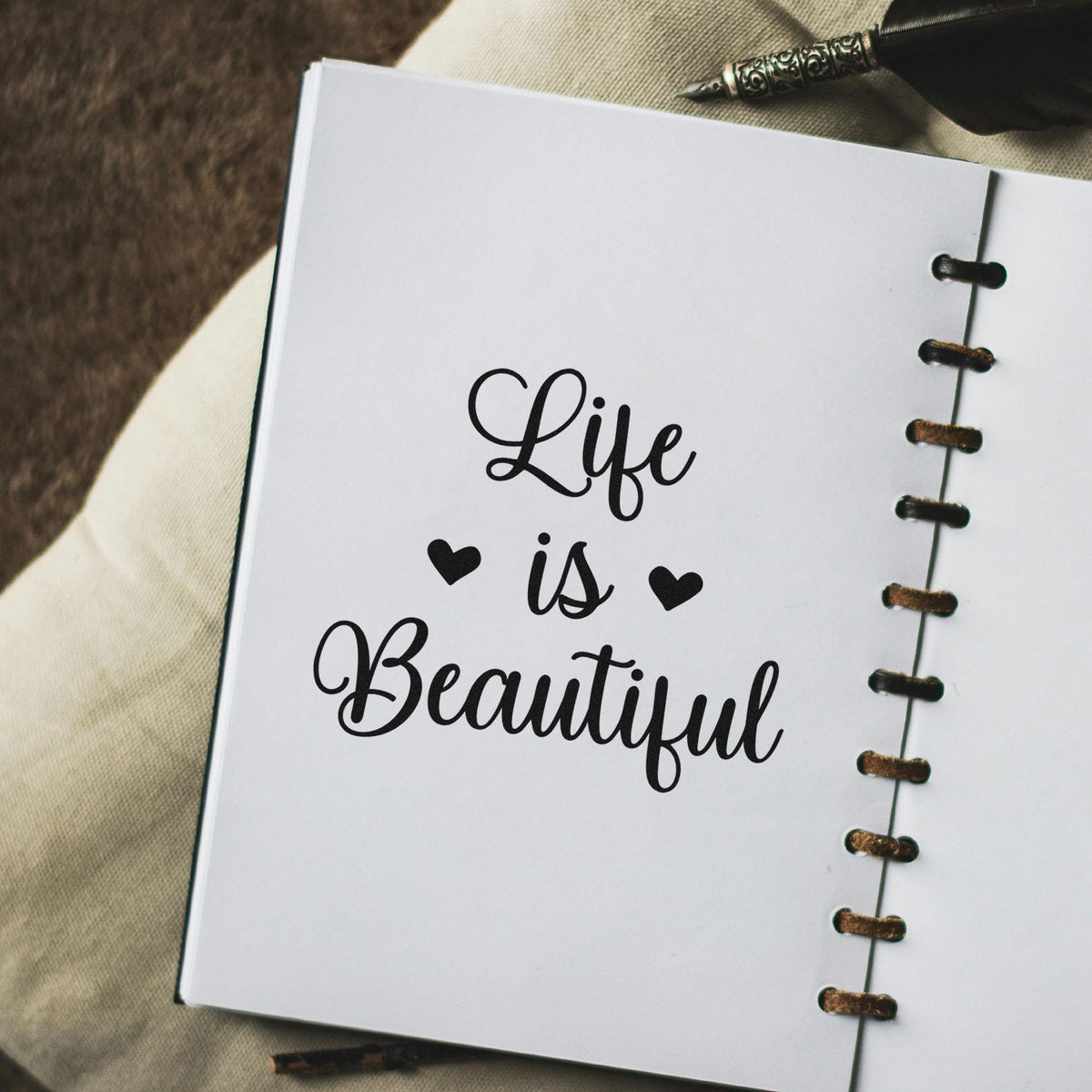 Black cursive Life is Beautiful stamp on a white notebook page with heart accents and bronze spiral binding.