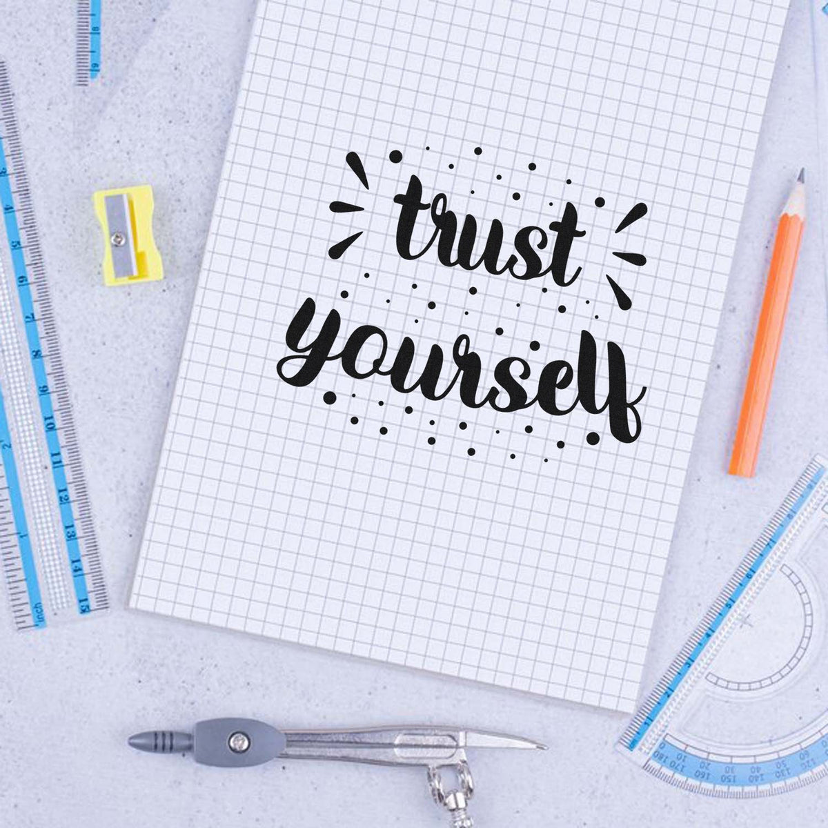 Black trust yourself rubber stamp on graph paper, with blue rulers, pencil, and compass.