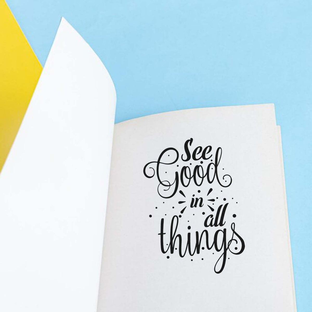 Black calligraphy stamp and seal reading See Good in all things on white paper with light blue background and yellow accent.