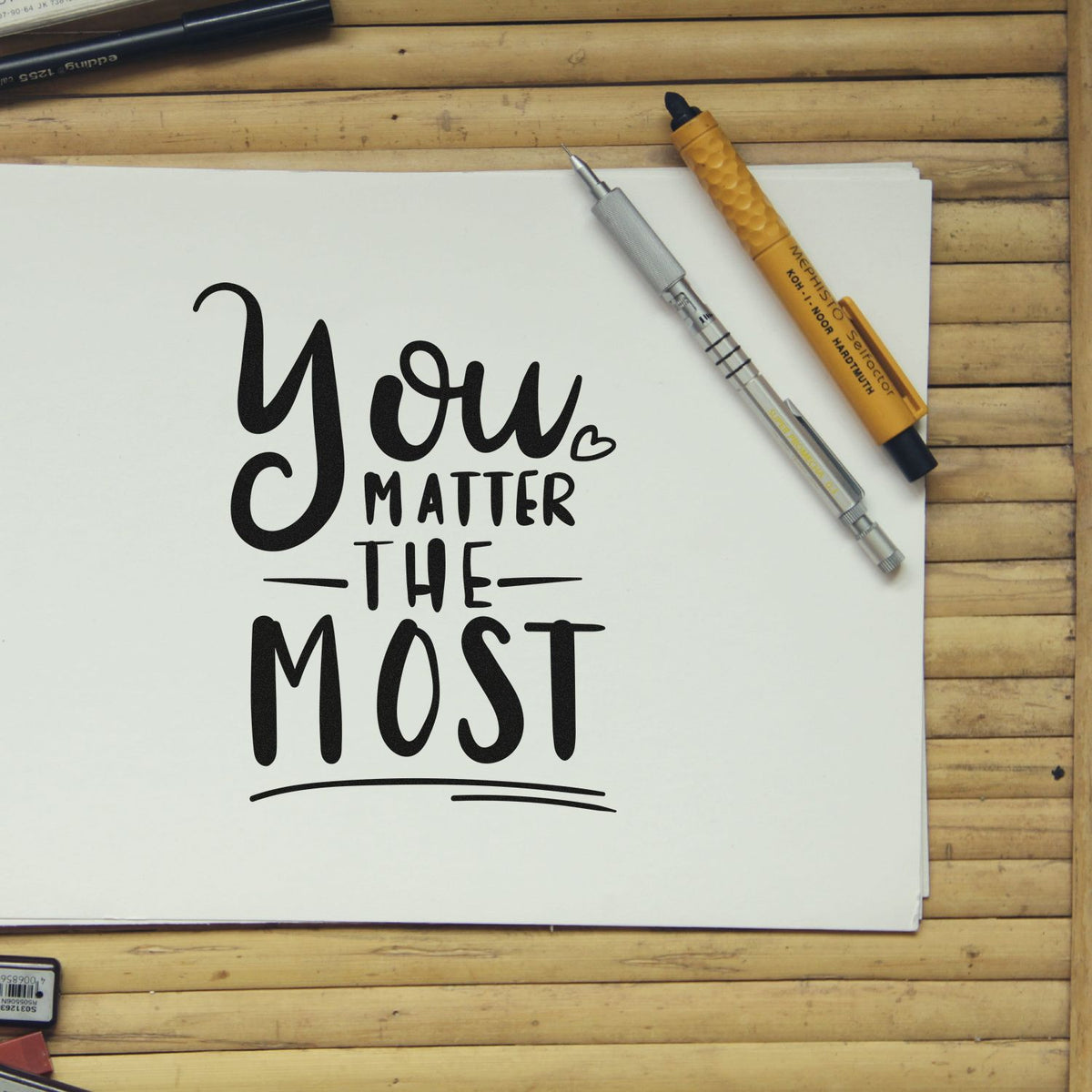 Black You Matter The Most calligraphy on white paper with silver and gold stamp-and-seal pens on a wooden desk.