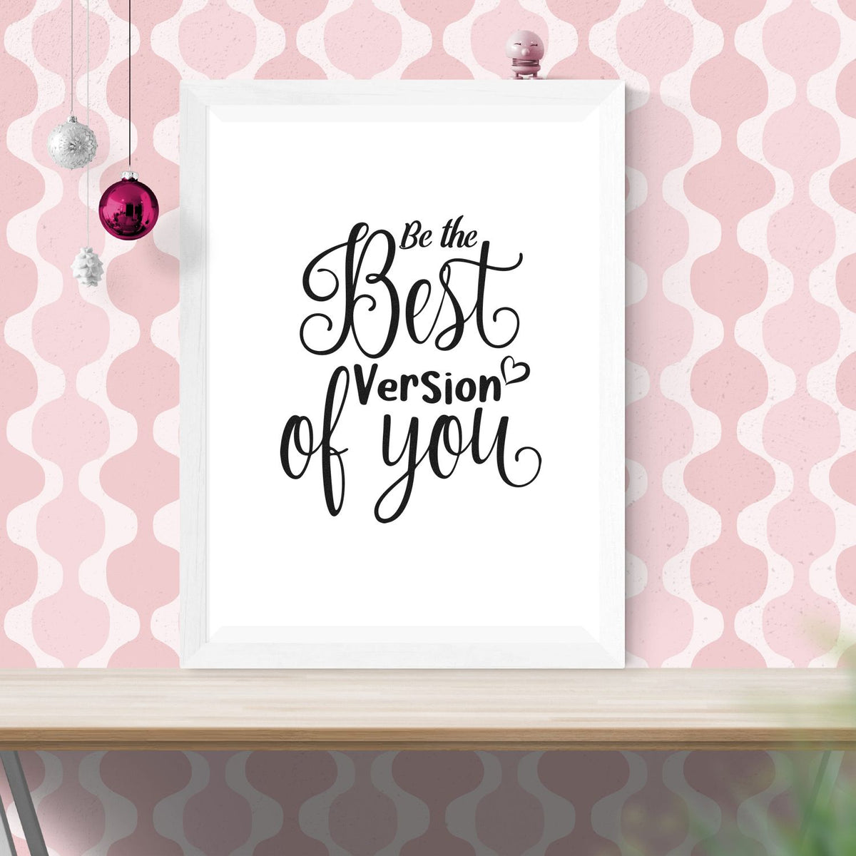Black script stamp and seal reading Be the Best Version of You on white frame, pink patterned background with hanging ornaments.