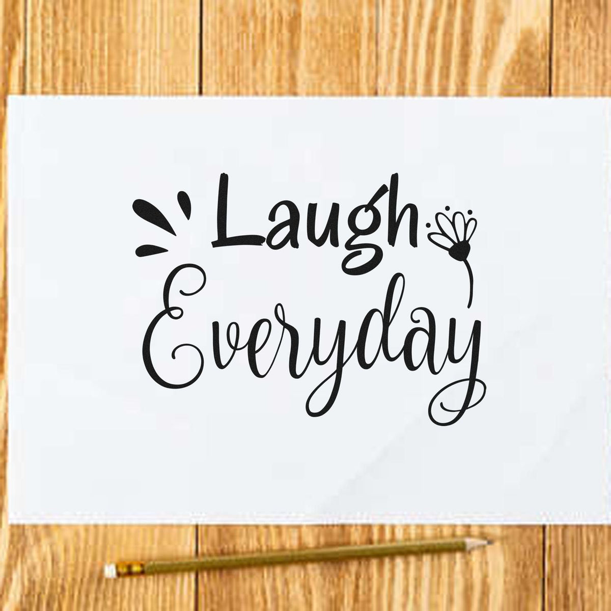 Black Laugh Everyday script stamp and floral seal on white paper over light wood?