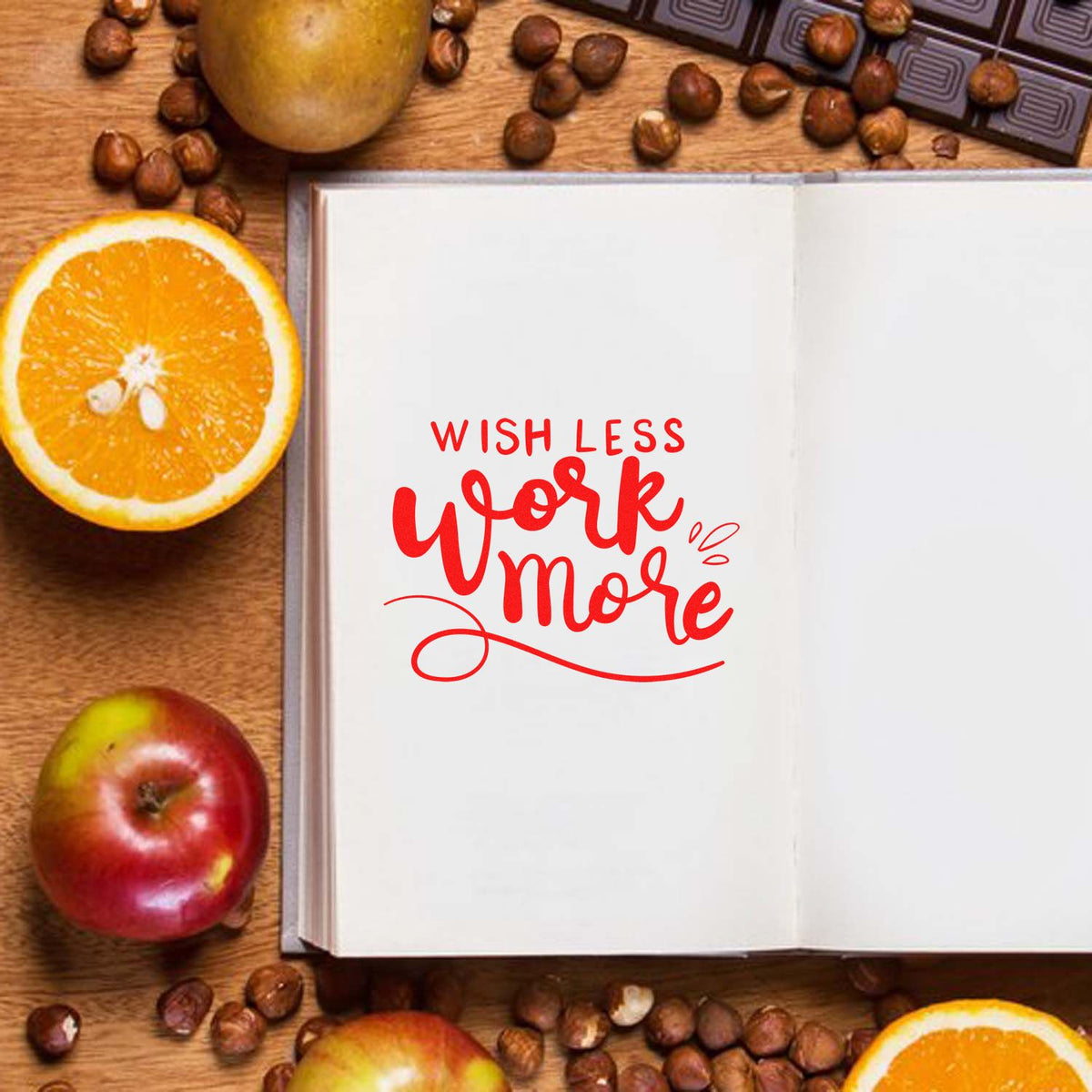Open notebook with red Wish Less Work More stamp seal, surrounded by oranges, apples, and coffee beans.