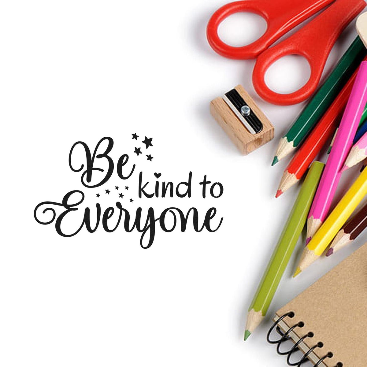 Black Be kind to Everyone stamp design with red scissors, wooden seal stamp, colorful pencils, and notebook on white background.