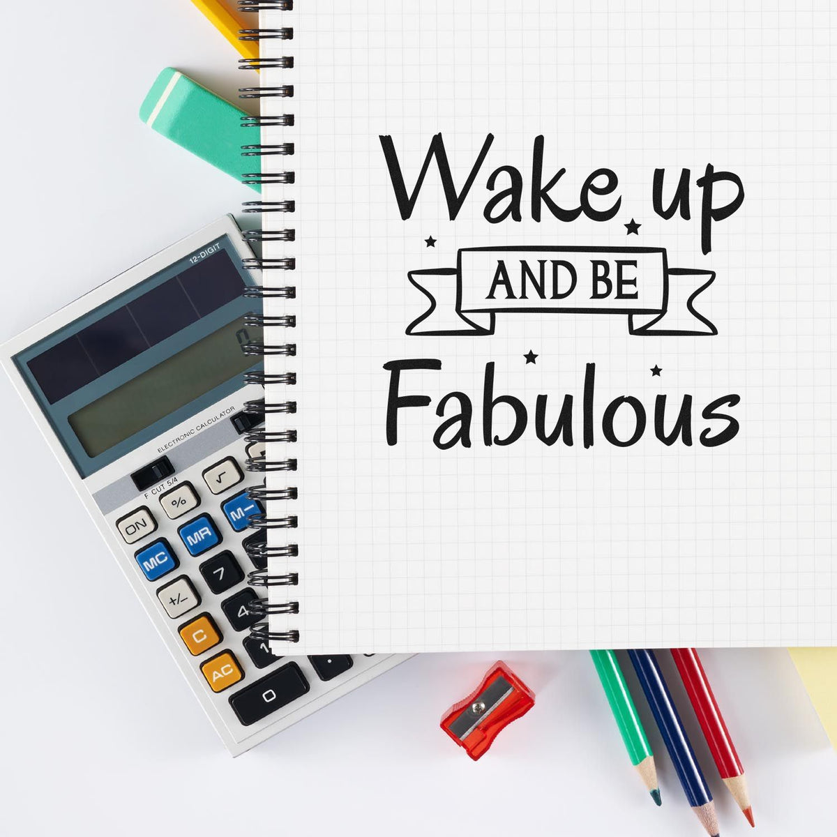 Black motivational stamp/seal on grid notebook with calculator, teal eraser, red sharpener, and colored pencils.