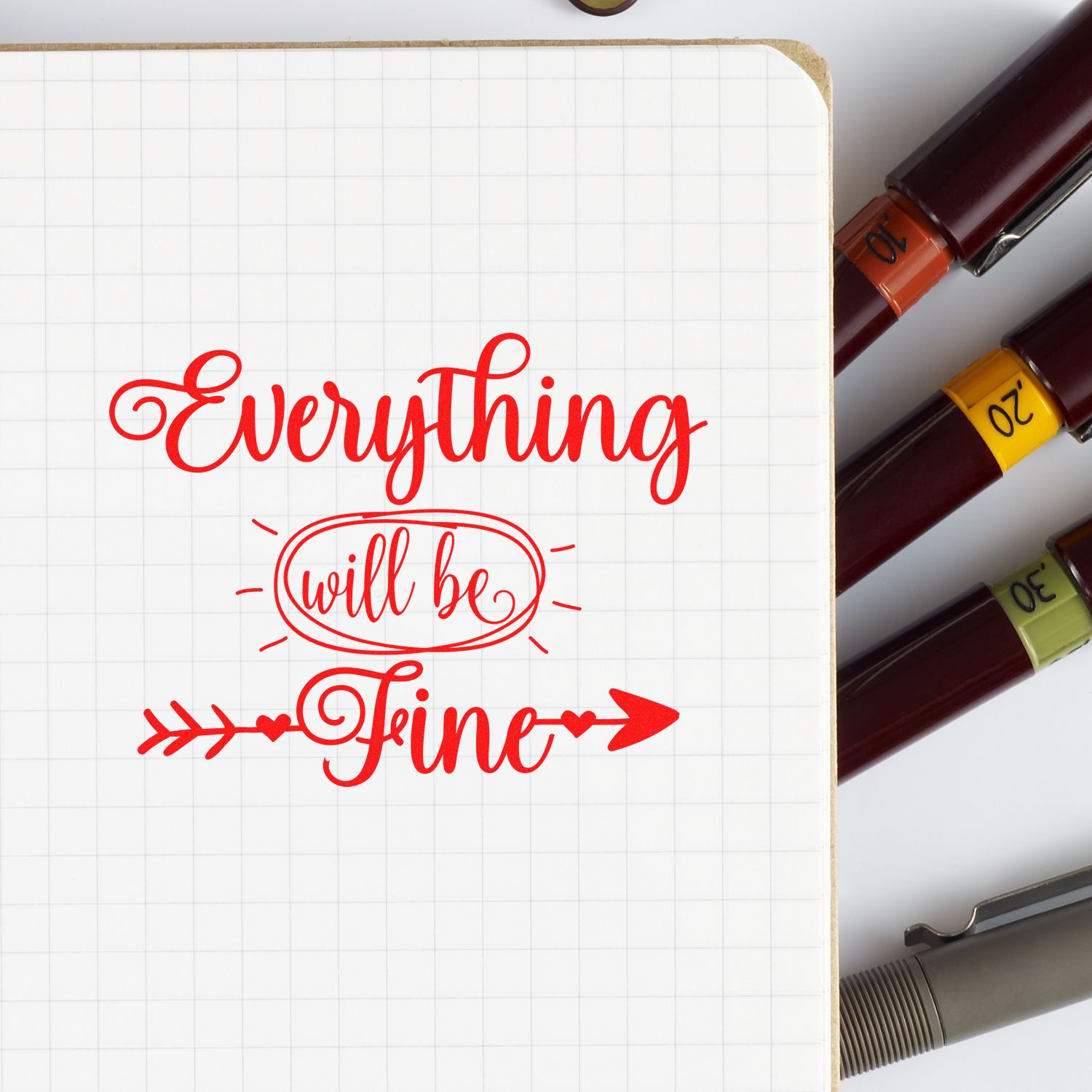 Grid notebook with red Everything will be Fine calligraphy stamp and maroon seal markers with orange, yellow, and green bands.