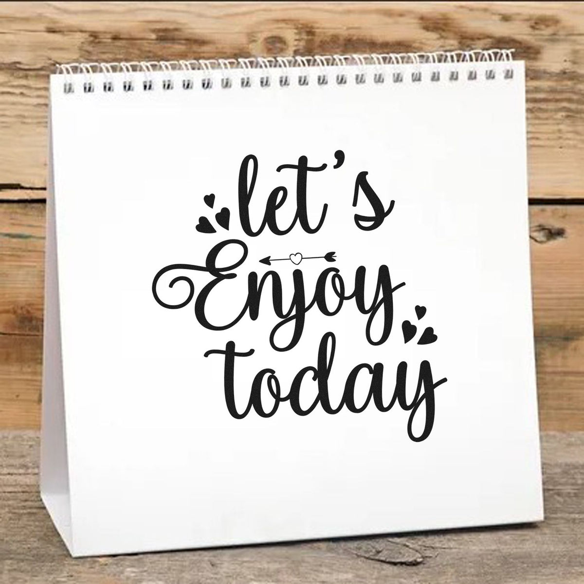 White paper bag with black custom stamp and seal design reading lets Enjoy today, with hearts on rustic wood.