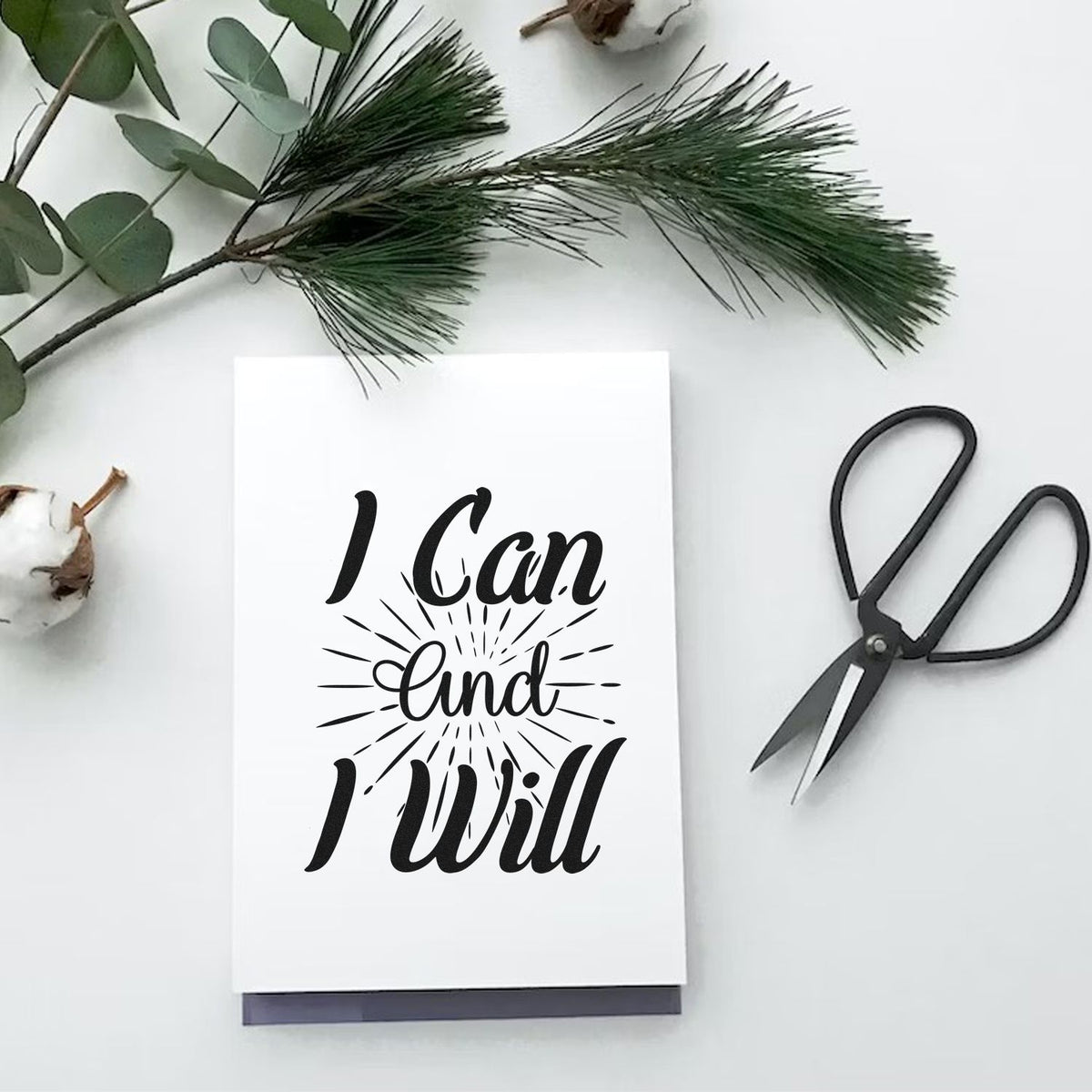 Black custom stamp and seal design reading I Can and I Will on a white card, with greenery and black scissors.