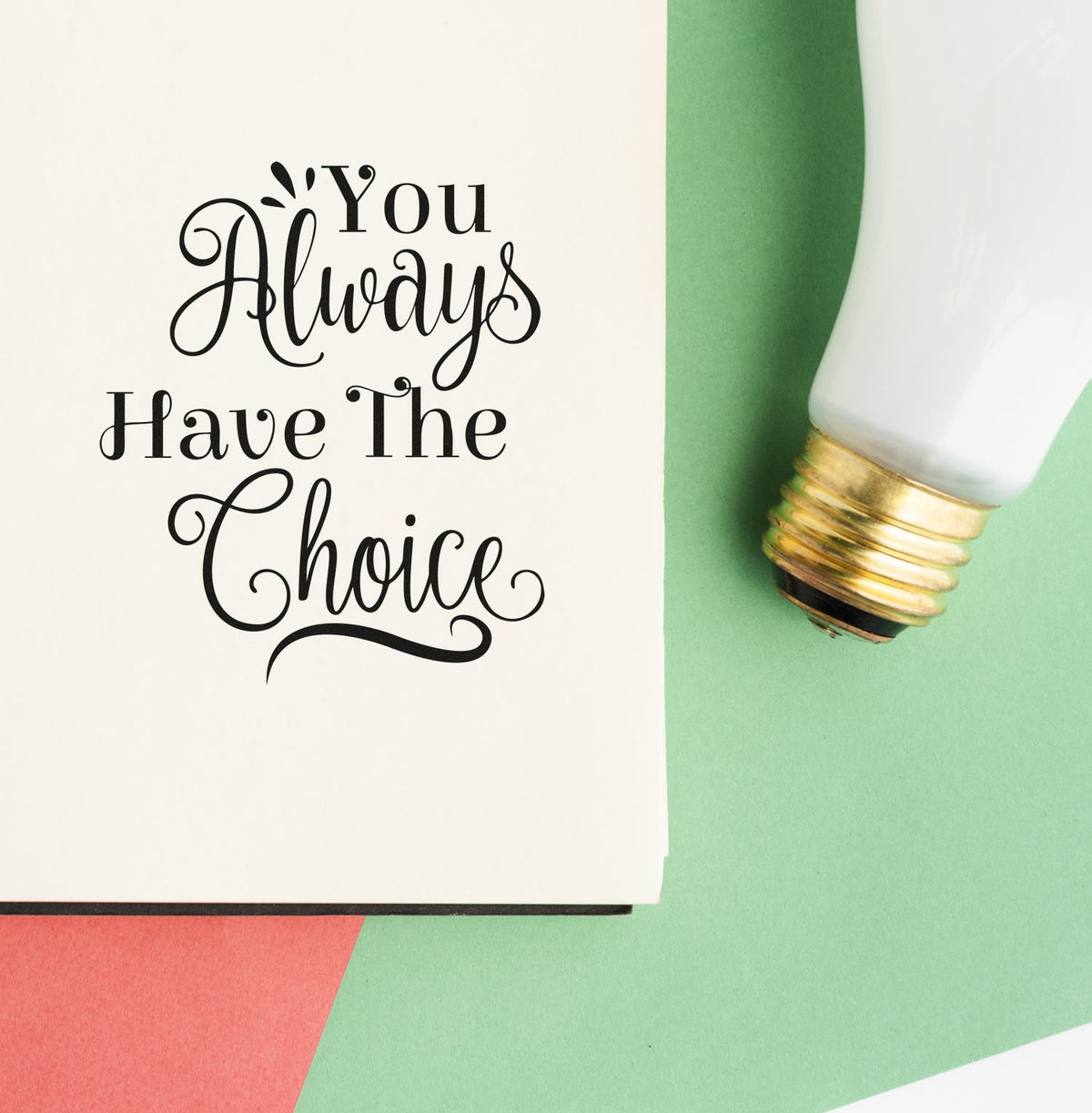 Black calligraphy stamp reading You Always Have The Choice beside a white-and-gold seal tube on green and cream paper.