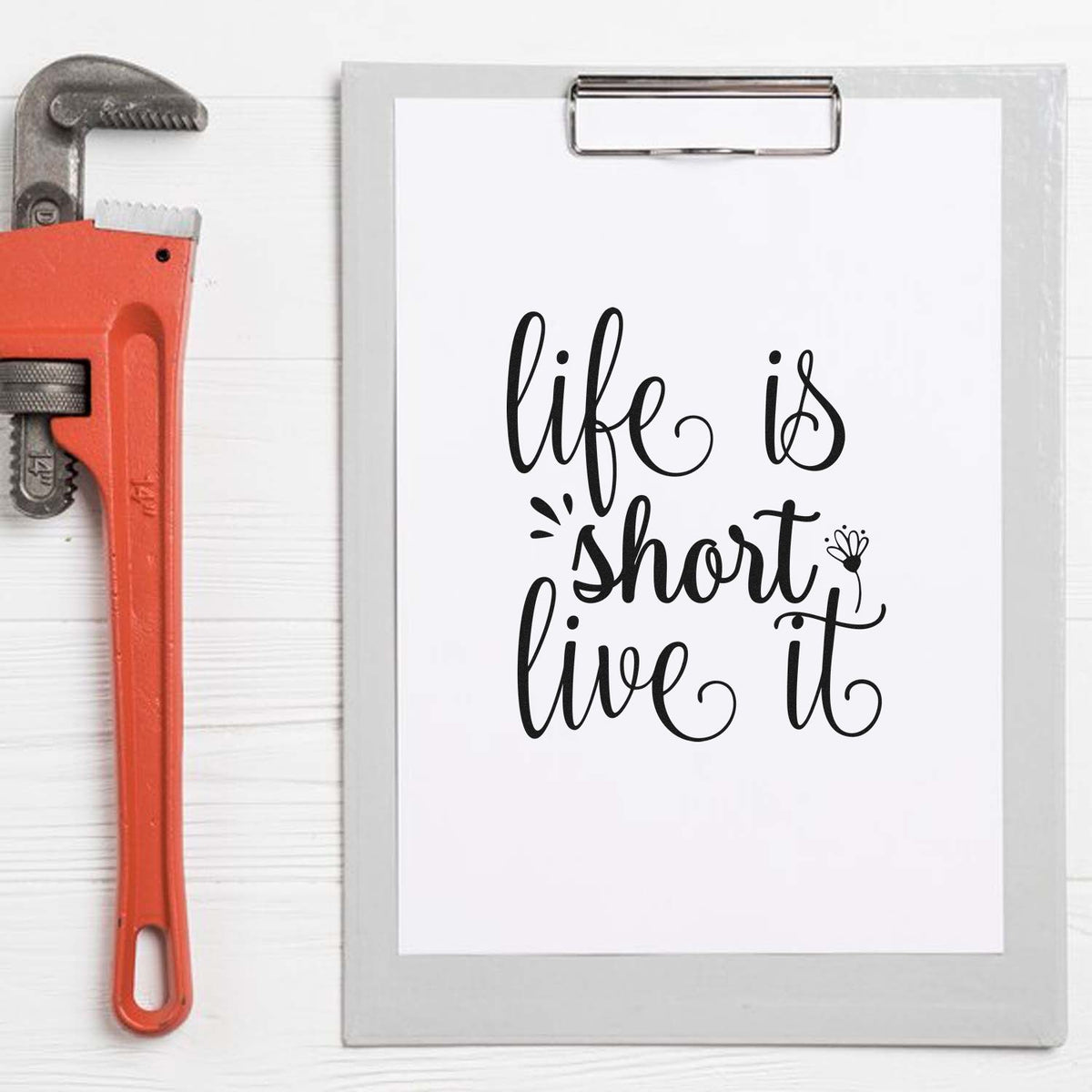 Orange stamp-and-seal tool beside a clipboard with white paper and black life is short, live it script.