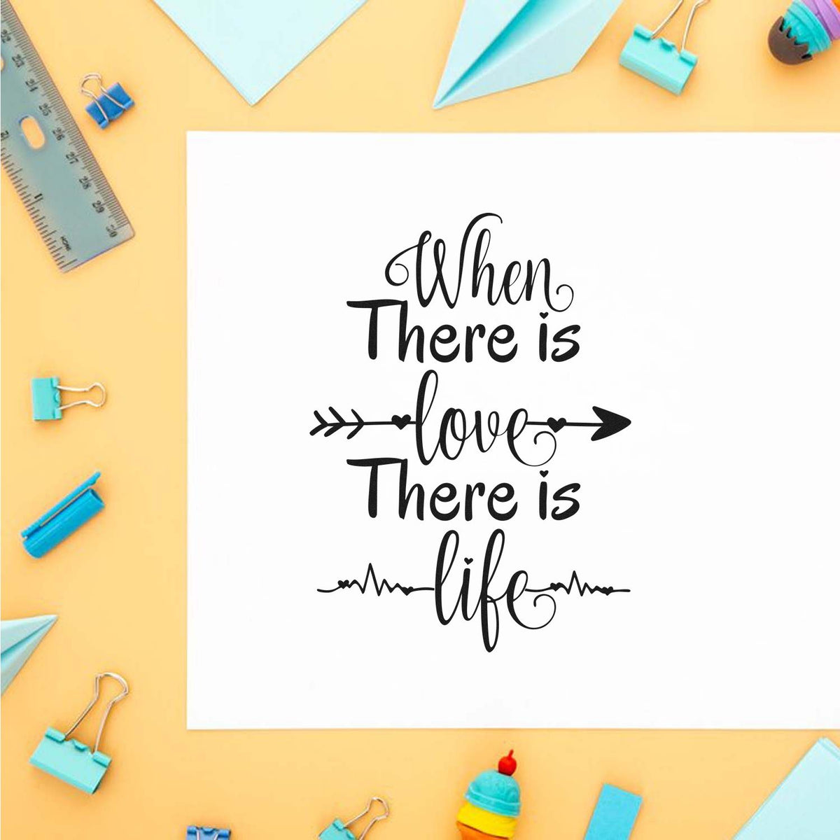 Decorative stamp design with black When There is love There is life quote, blue clips, ruler, and paper planes on yellow.