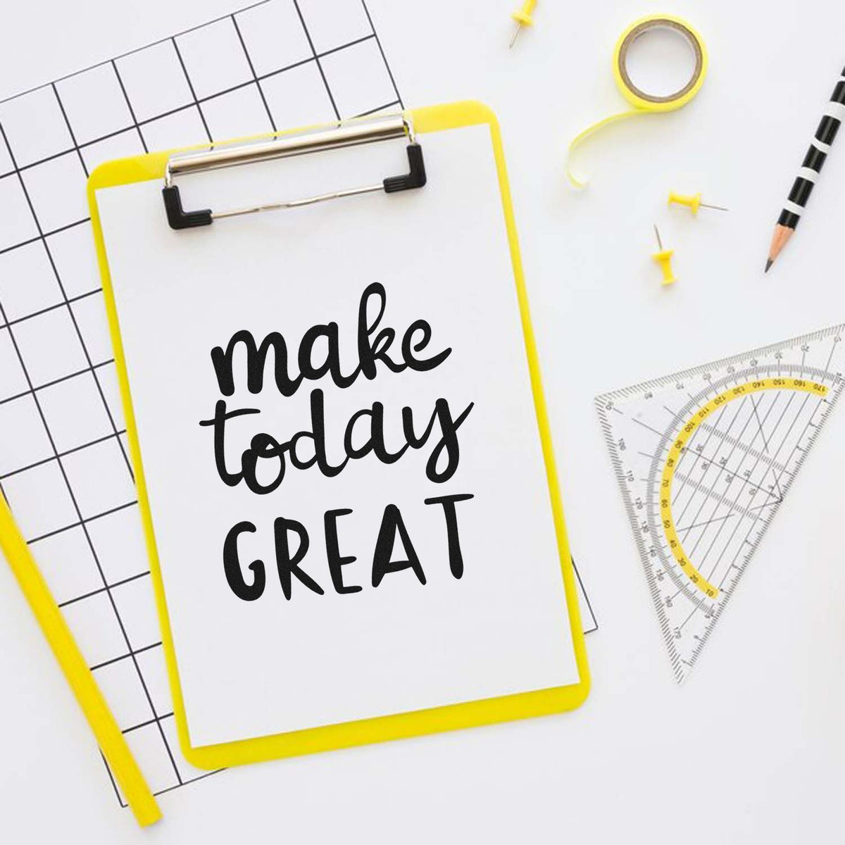 Yellow custom stamp/seal clipboard with make today GREAT on white paper, surrounded by grid paper, tape, pins and ruler.