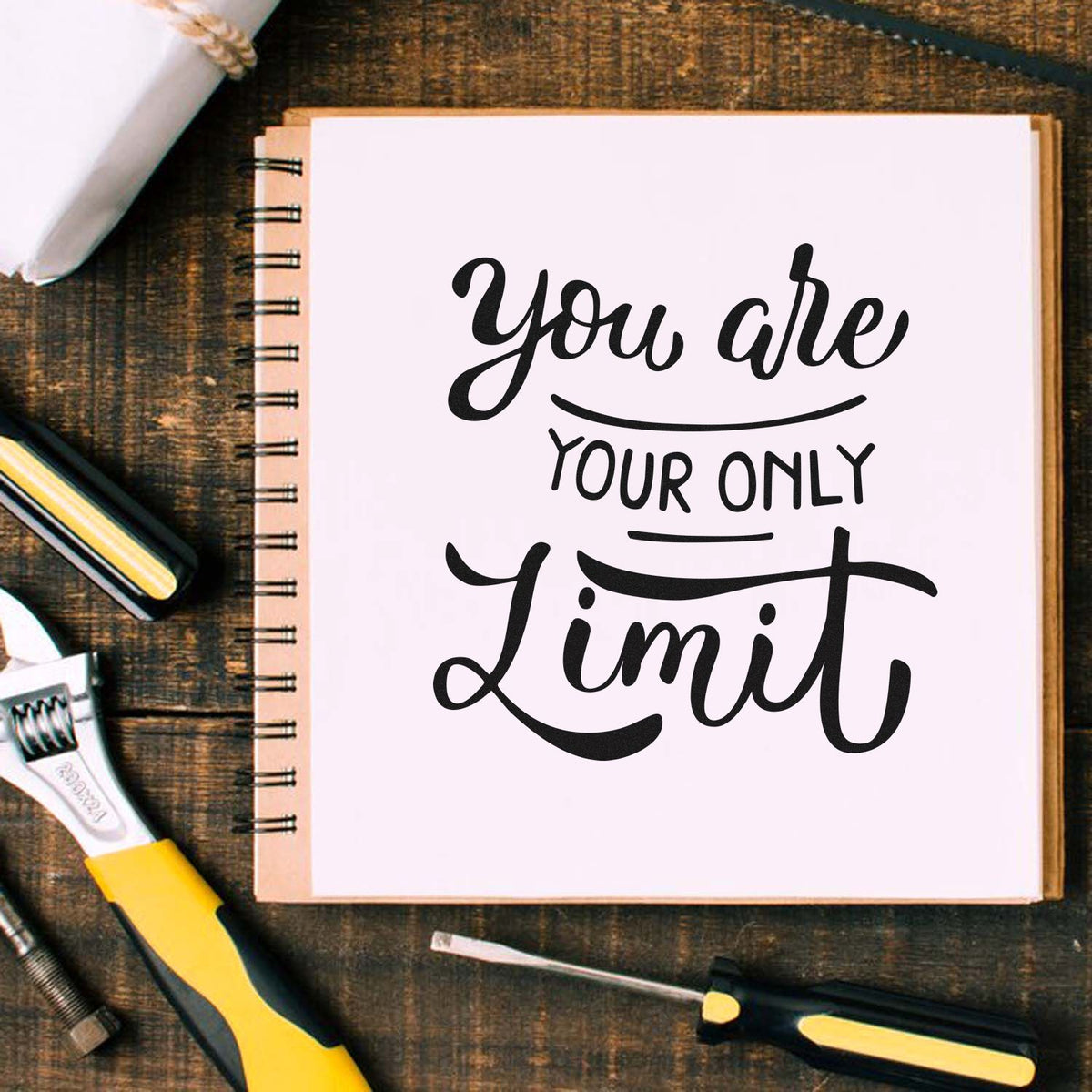 Black and yellow stamp and seal tools around a spiral notebook reading You are your only limit on rustic wood.
