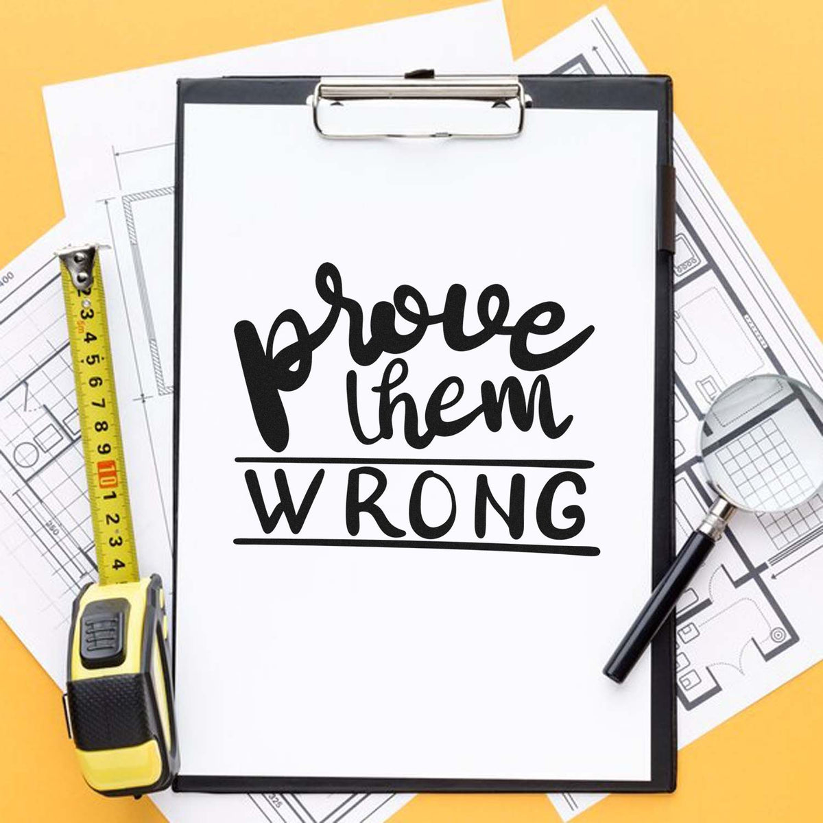 Black custom stamp and seal reading prove them wrong on clipboard, with yellow tape measure, magnifier, and blueprints.