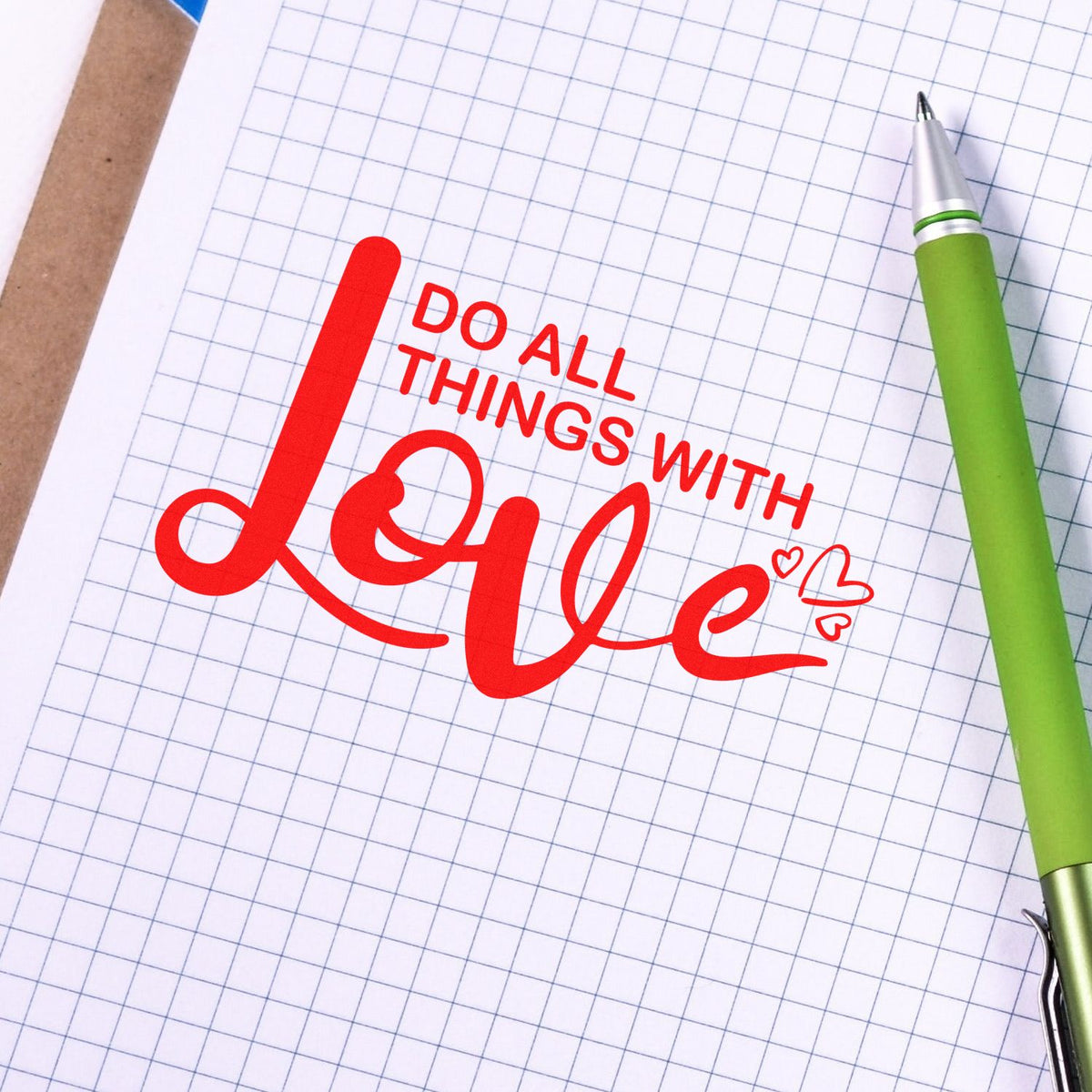 Red Do all things with love stamp on graph paper beside a green pen, highlighting stamp and seal products.