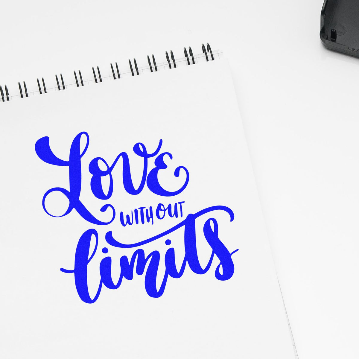 Blue Love without limits stamp on a white spiral notebook, with a black stamp/seal case in the corner.