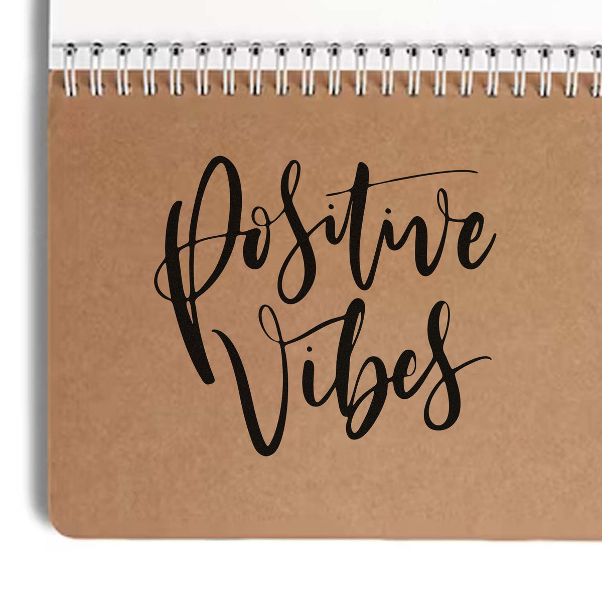 Black Positive Vibes stamp and seal on a brown kraft spiral notebook cover with white coil binding