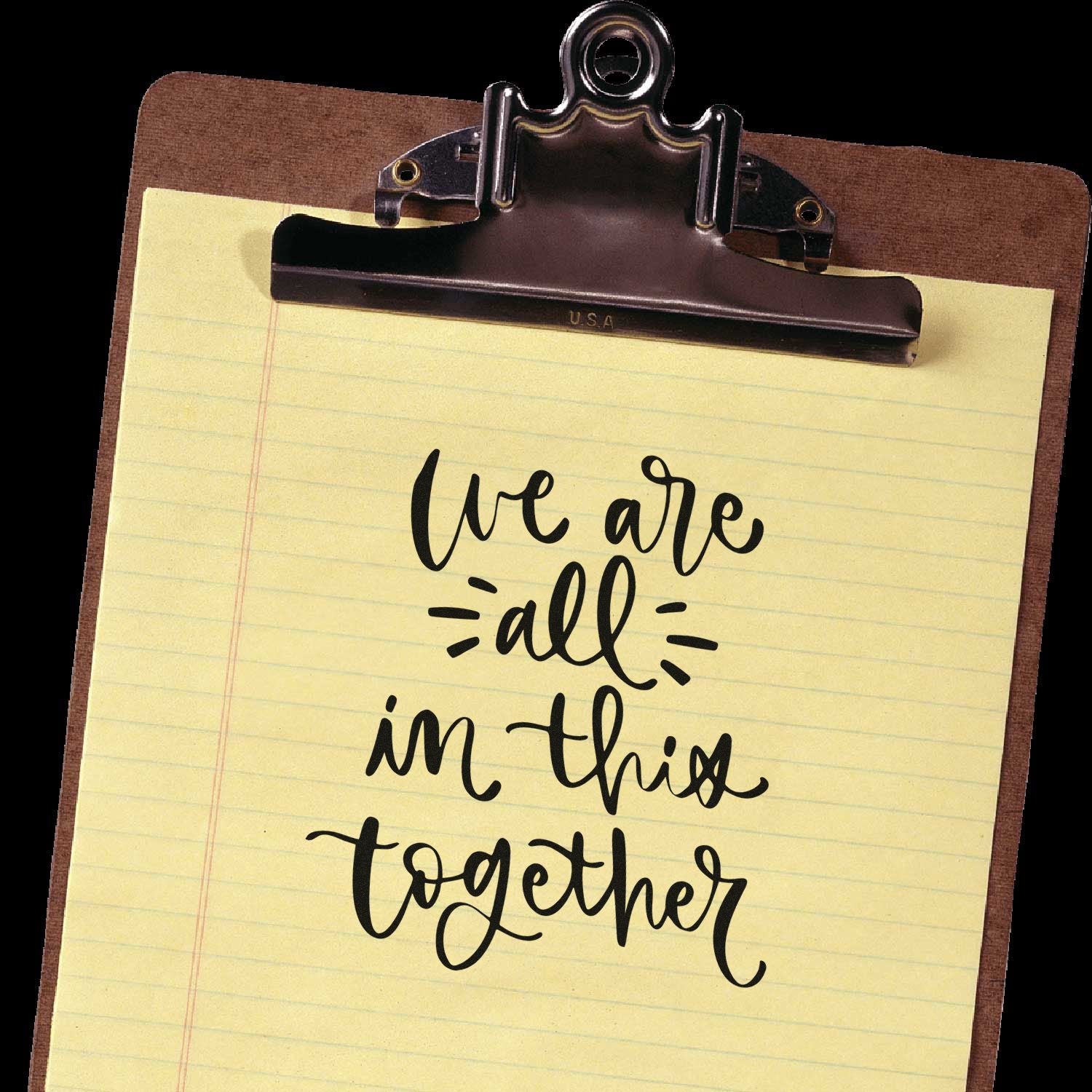 Clipboard with custom stamp and seal design on yellow lined paper, featuring black handwritten we are all in this together text.