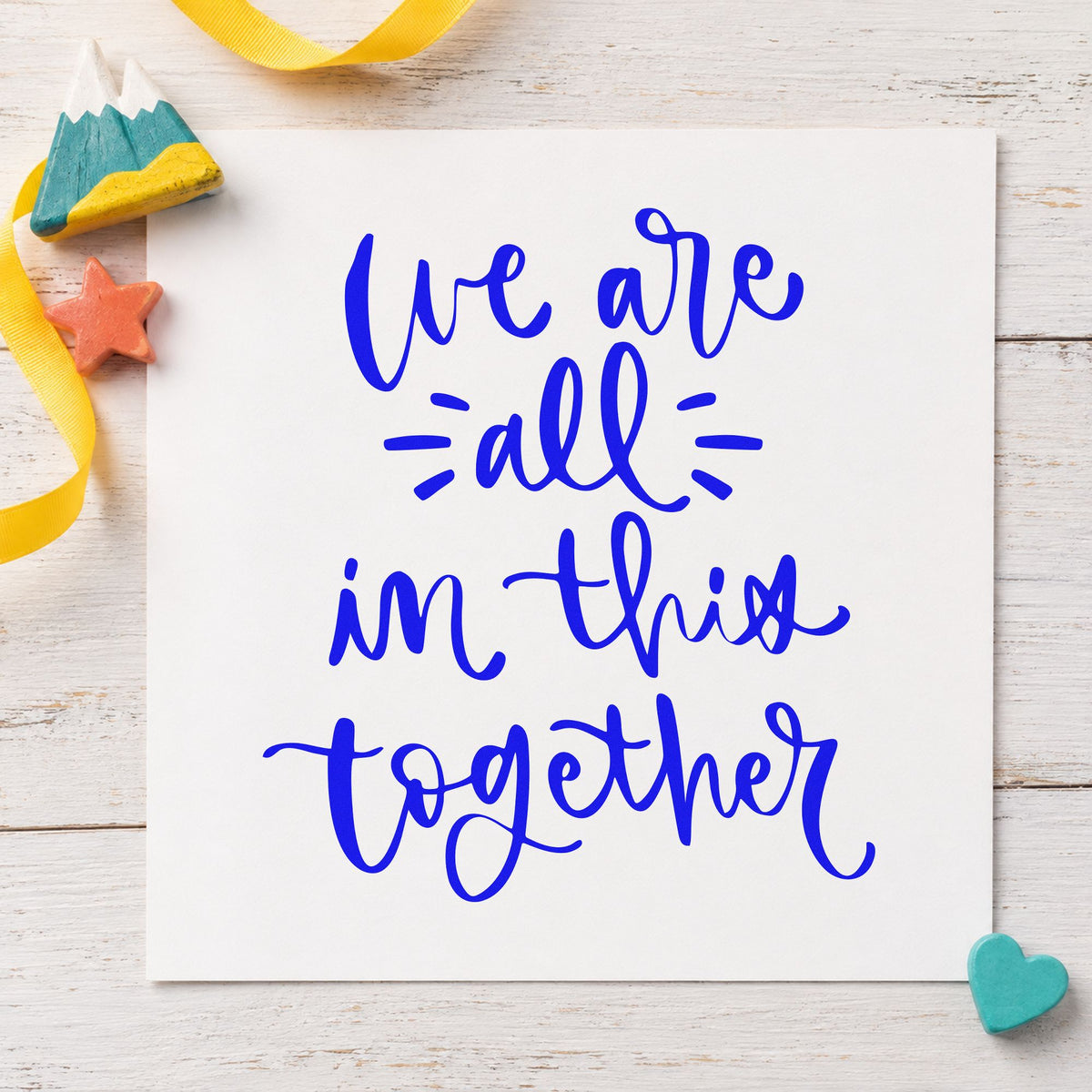We Are All In Together craft stamp imprinted in blue ink on paper, a design suited to framed community board.