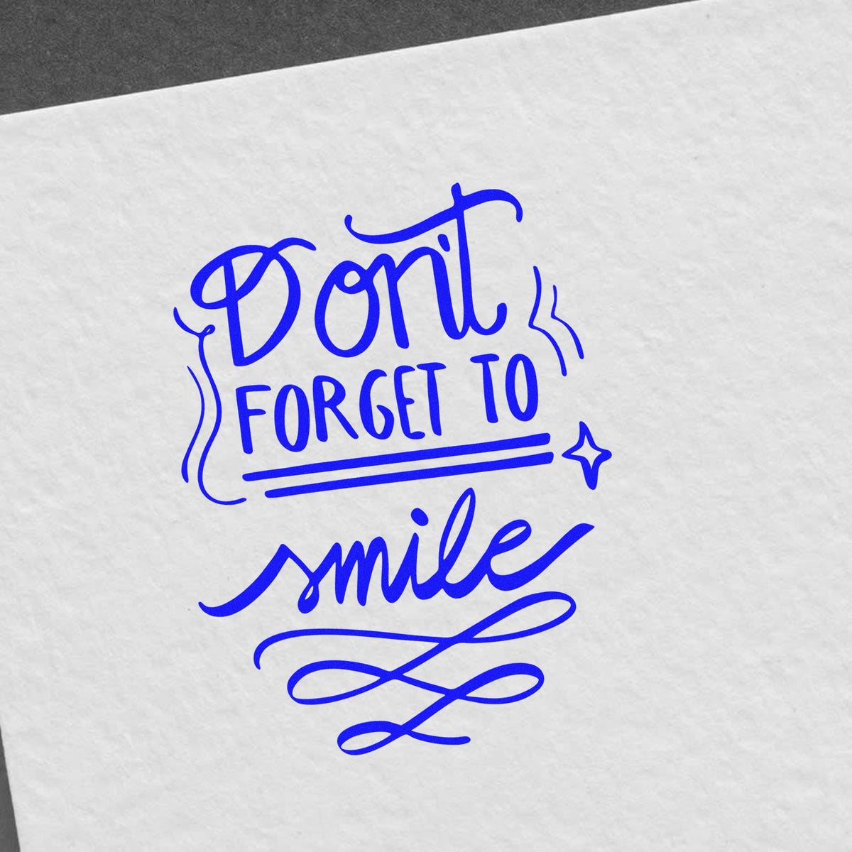 Blue stamp seal with Dont forget to smile lettering and decorative flourishes on white paper