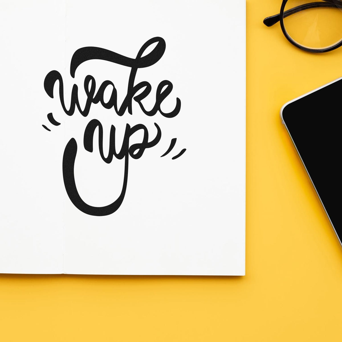 Black Wake Up stamp seal on white paper, with yellow background, eyeglasses and smartphone.