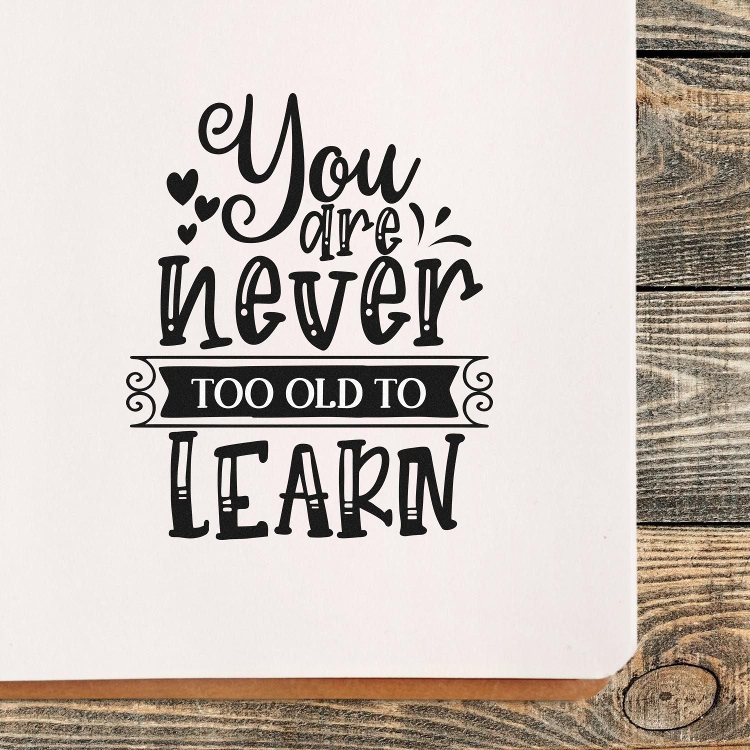 Black decorative stamp/seal with hearts and You are never too old to learn on white card over rustic wood.
