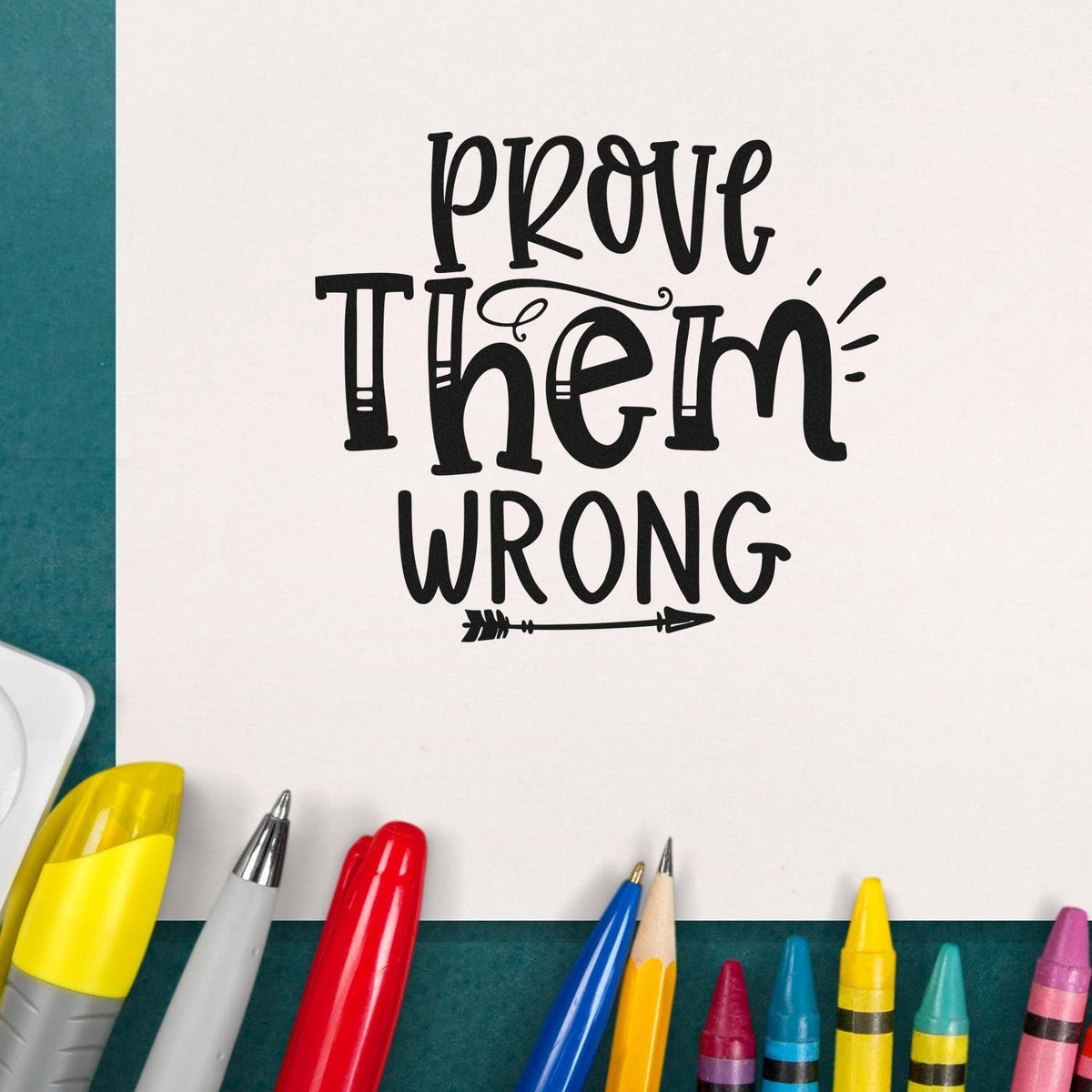 Custom stamp and seal design reading Prove Them Wrong in black on white paper, surrounded by colorful pens and markers.