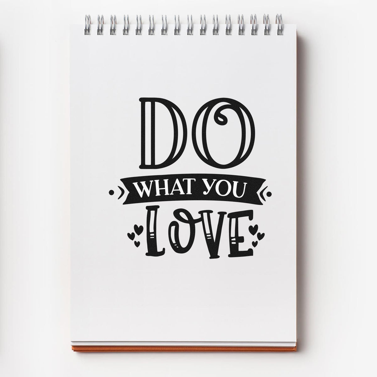 Black Do What You Love stamp and seal design on a white spiral notebook, with bold lettering, a banner, and small hearts.