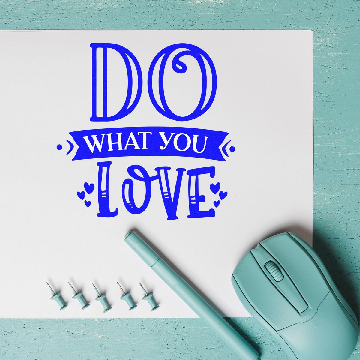 Blue Do what you love stamp design with hearts, mint seal tool, stylus, and pins on a white sheet over teal background.